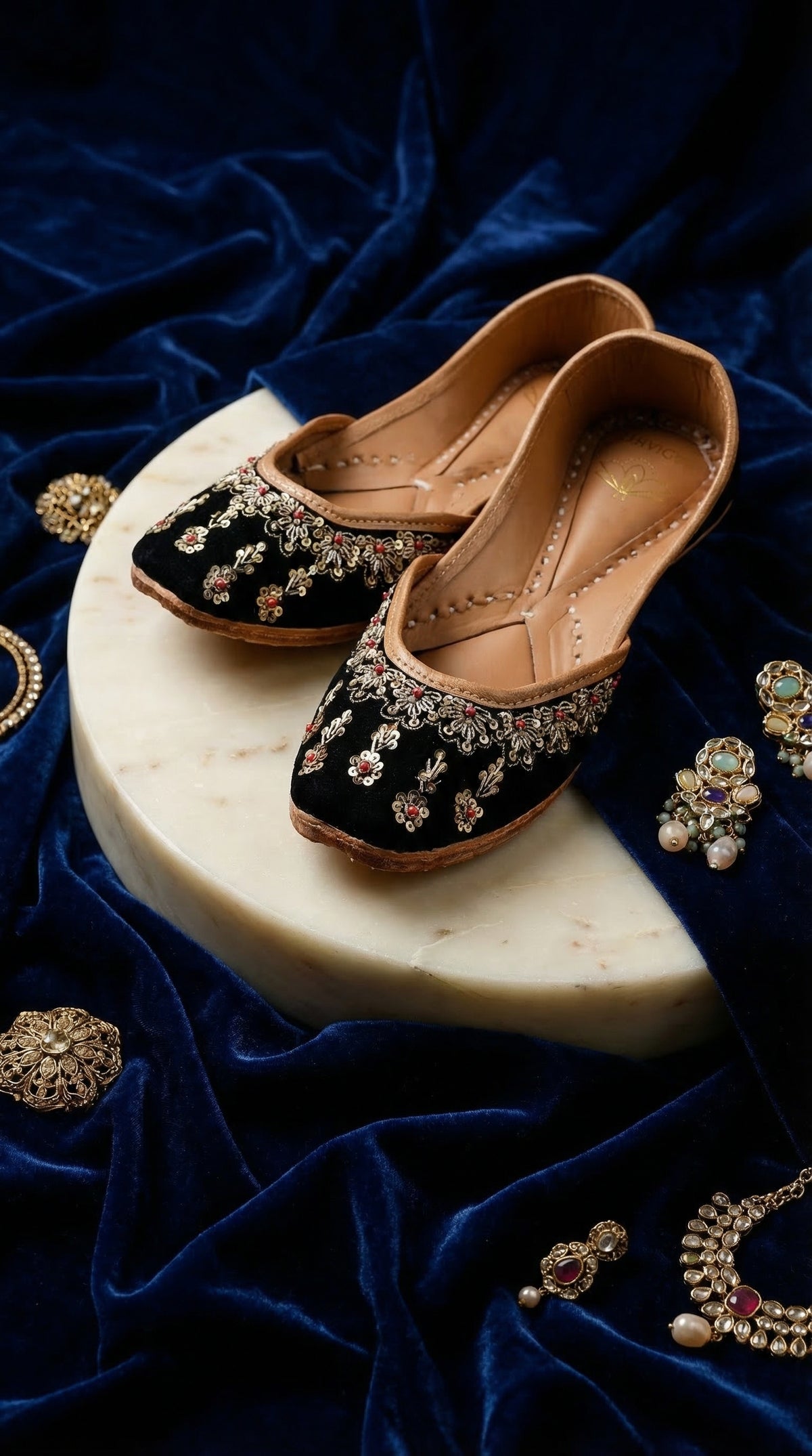 Zehra silver zardozi ruby jutti pair – on marble pedestal surrounded by navy velvet and kundan jewellery Radiarte