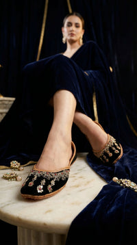 Zehra black velvet ruby embroidered jutti on feet – model in navy velvet outfit on marble in dramatic setting Radiarte