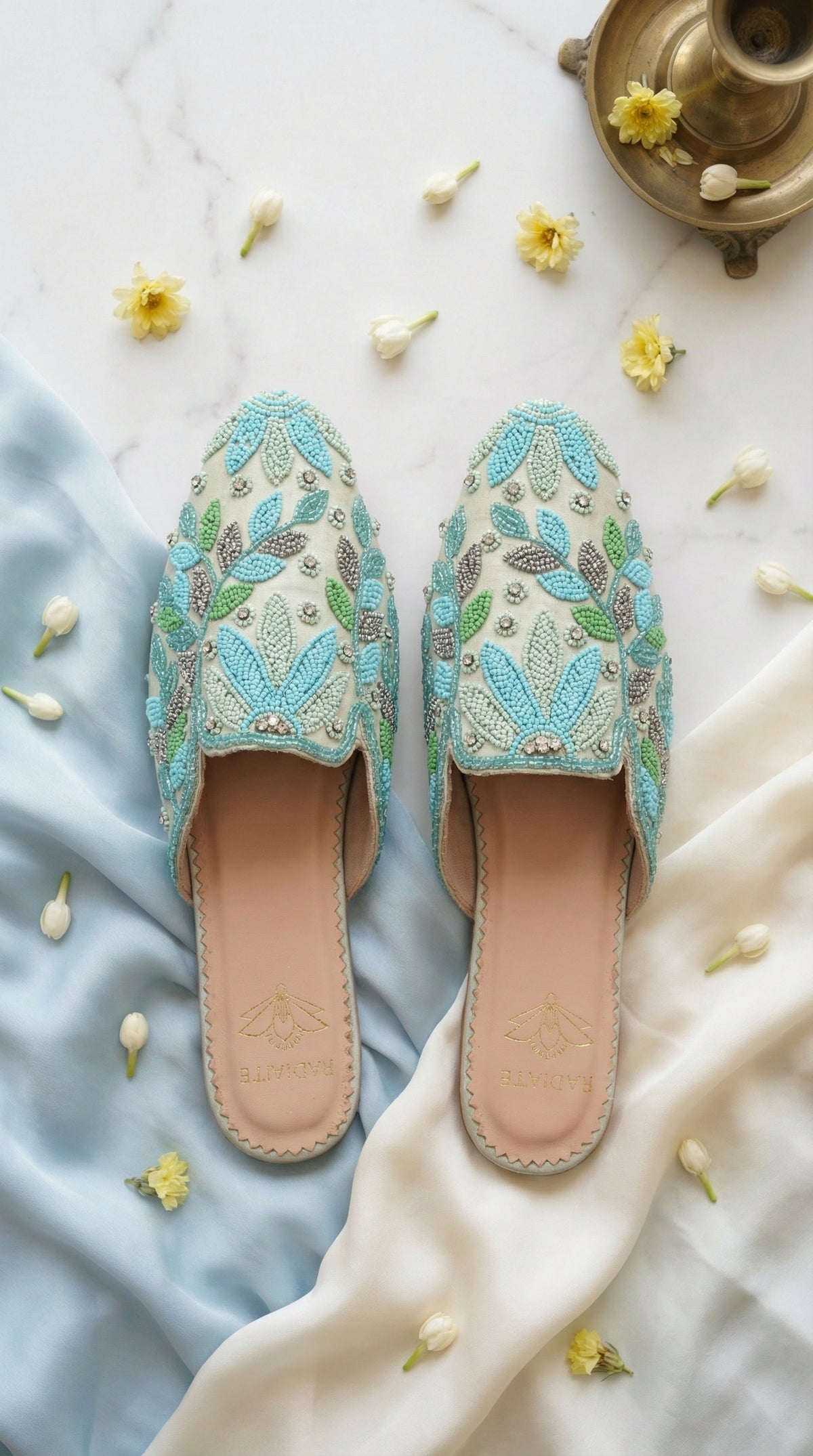 Whispering Skies sky blue beaded leaf mule flat by Radiarte – top view on marble with blue silk and yellow flowers