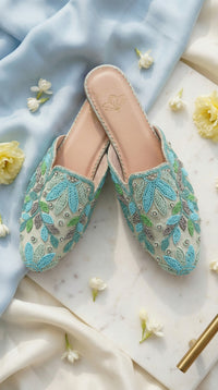 Whispering Skies handcrafted seed bead mule flat pair – side view on marble with blue drape and white blooms Radiarte