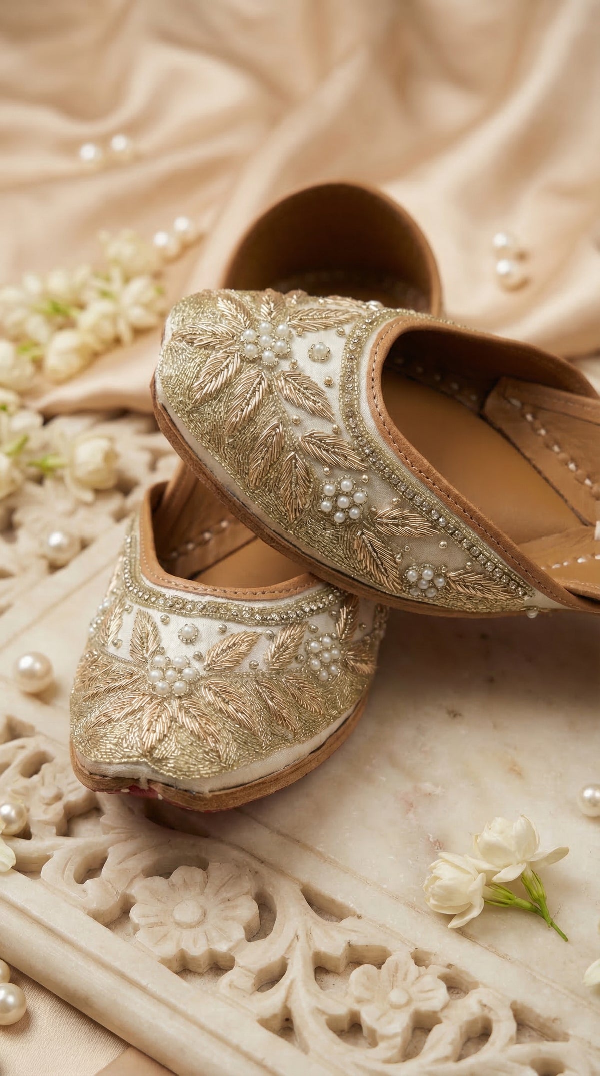 Tara ivory gold embroidered jutti pair – close-up of zardozi leaf motifs and pearl rosettes on carved marble tray