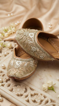 Tara ivory gold embroidered jutti pair – close-up of zardozi leaf motifs and pearl rosettes on carved marble tray