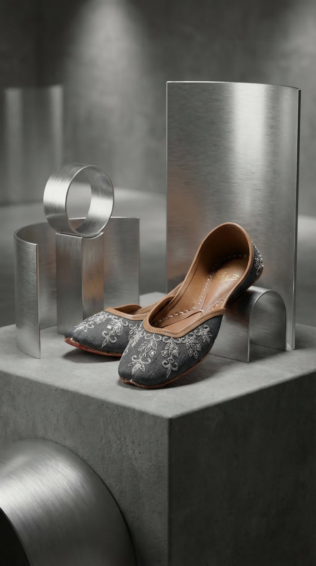 Saanjh grey silver embroidered jutti by Radiarte – pair on concrete pedestal with brushed steel sculptures