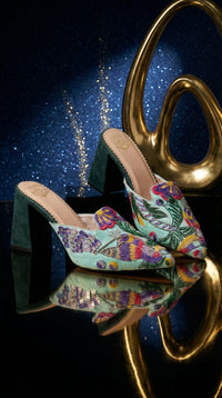 Rio handcrafted multicolour embroidered block heel mule – side view on reflective surface with gold sculpture