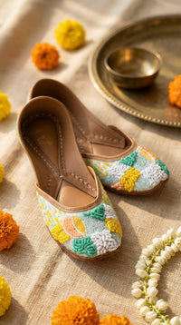Zale handcrafted raised embroidery pastel jutti pair – side view on linen with marigolds and brass thali Radiarte