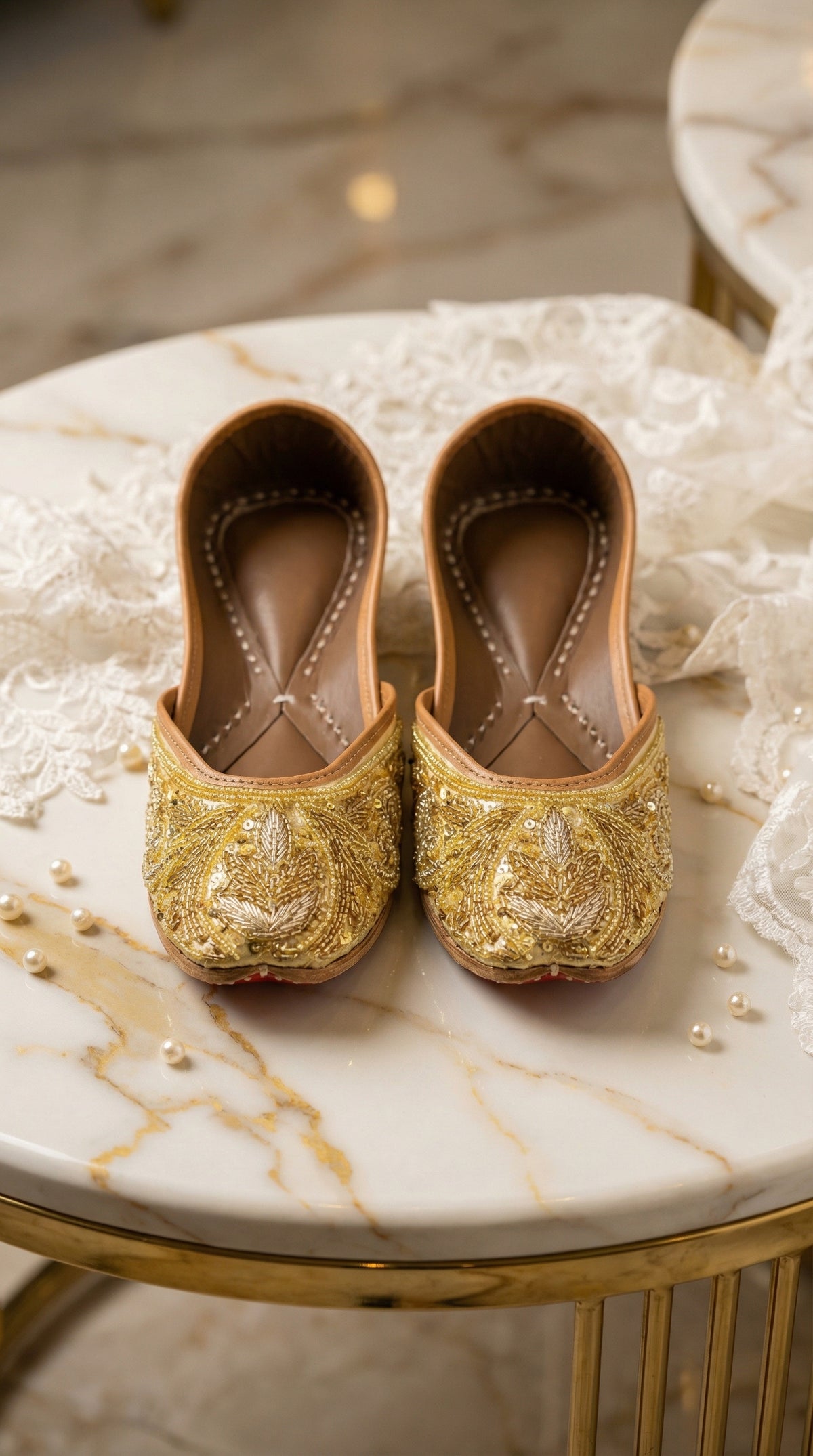Shararat gold bugle bead jutti pair – front view on marble side table with ivory lace by Radiarte