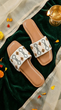 Taj white beaded slide flat – top view display on green velvet with brass diya and marigold petals Radiarte